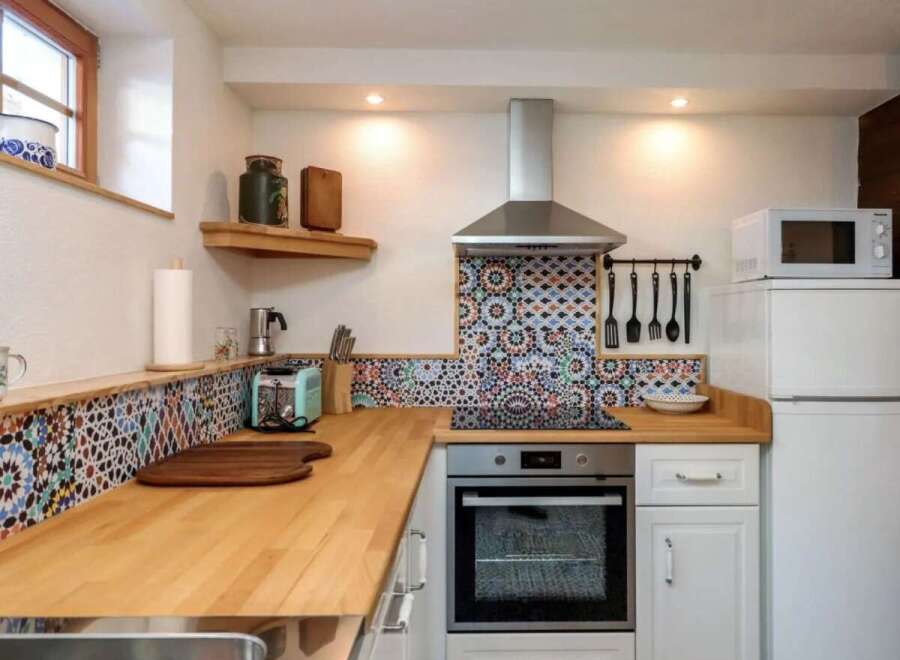 This charming kitchen features a unique mosaic backsplash and warm wooden countertops, creating a cozy and inviting atmosphere.