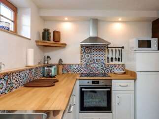 This charming kitchen features a unique mosaic backsplash and warm wooden countertops, creating a cozy and inviting atmosphere.