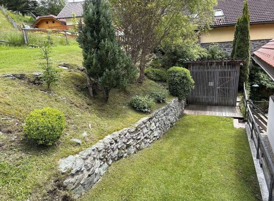 Discover a charming property with a beautifully landscaped garden, featuring a stone retaining wall and lush greenery.