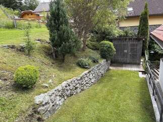 Discover a charming property with a beautifully landscaped garden, featuring a stone retaining wall and lush greenery.