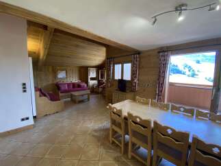 This charming chalet boasts a spacious open-plan living area with a comfortable sofa and a large dining table perfect for family gatherings.