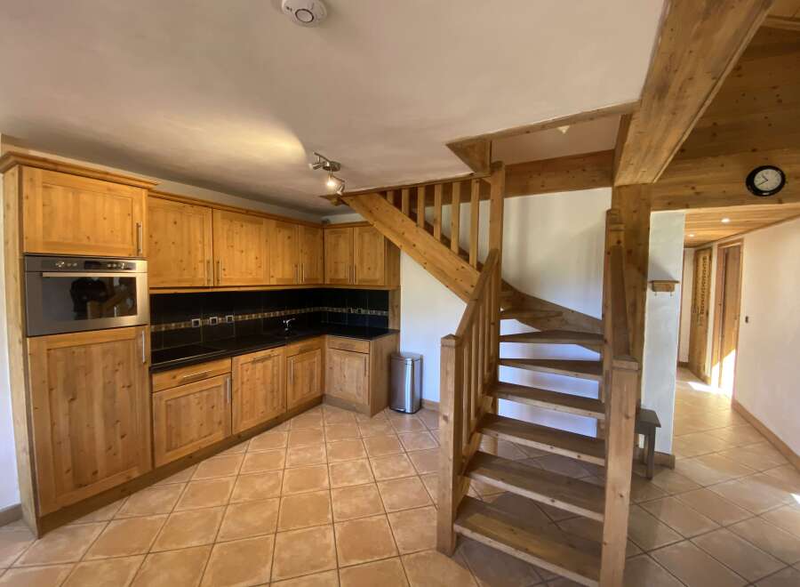 This charming chalet boasts a rustic kitchen with light wood cabinets and a tiled floor, creating a warm and inviting atmosphere.