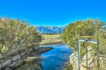Serene landscape featuring a tranquil stream flowing through a natural setting, with snow-capped mountains in the background.