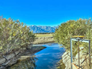 Serene landscape featuring a tranquil stream flowing through a natural setting, with snow-capped mountains in the background.