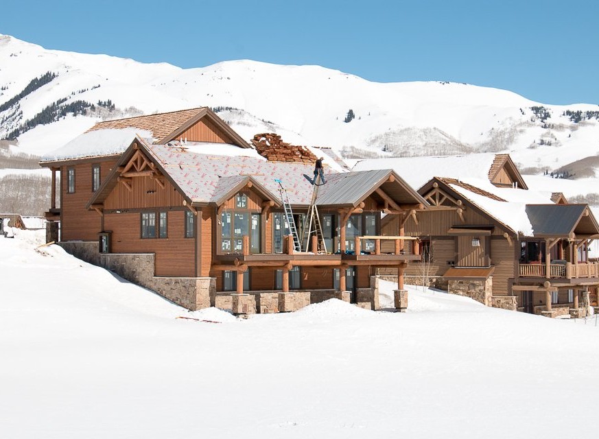 Luxury mountain home undergoing roof construction in a stunning snowy landscape.