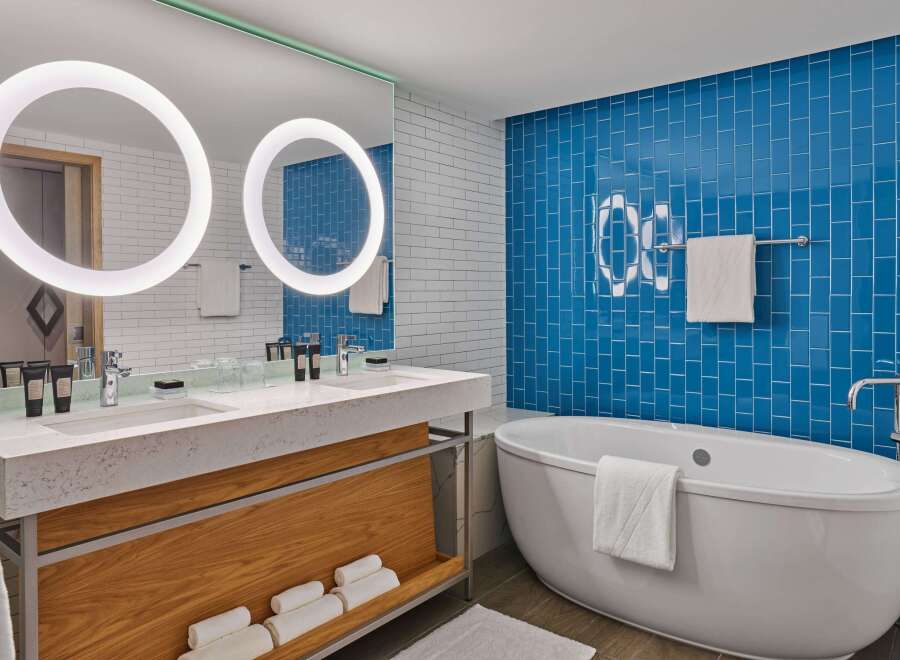 This luxurious bathroom boasts a double vanity with a marble countertop, modern double circular mirrors, and ample storage.