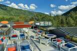 This rooftop patio boasts stunning mountain views, comfortable seating areas with vibrant orange and blue pillows, and a fire pit for cozy gatherings.
