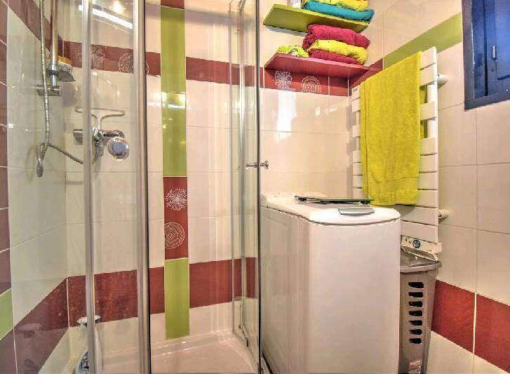 This charming bathroom boasts a modern shower enclosure, a convenient washer, and stylish storage shelves.