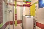 This charming bathroom boasts a modern shower enclosure, a convenient washer, and stylish storage shelves.