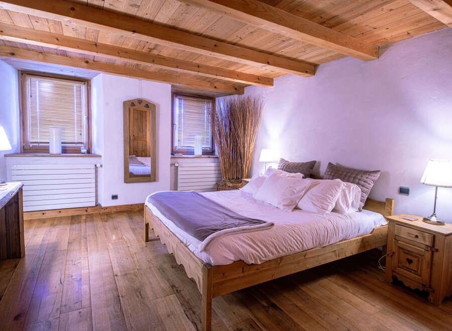 Cozy chalet bedroom with wooden beams, hardwood floors, and a comfortable bed.