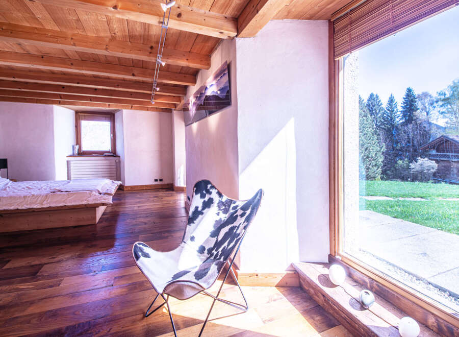 This stunning bedroom boasts a rustic-chic design with exposed wooden beams, hardwood floors, and large windows offering breathtaking views.