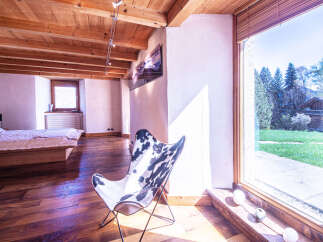 This stunning bedroom boasts a rustic-chic design with exposed wooden beams, hardwood floors, and large windows offering breathtaking views.