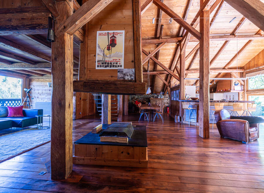 This stunning chalet boasts a spacious open-plan living area with exposed wooden beams and a large stone fireplace, creating a warm and inviting atmosphere.