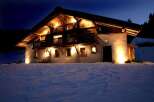This stunning chalet boasts a beautiful wooden exterior, illuminated at night, creating a warm and inviting atmosphere.
