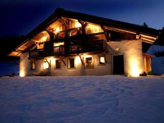 This stunning chalet boasts a beautiful wooden exterior, illuminated at night, creating a warm and inviting atmosphere.