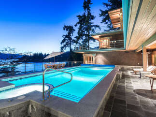 Luxury waterfront property featuring a stunning infinity pool and hot tub, perfect for enjoying breathtaking sunset views.