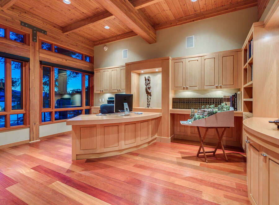 This stunning home office boasts a curved wooden desk, built-in bookshelves, and large windows offering breathtaking views.