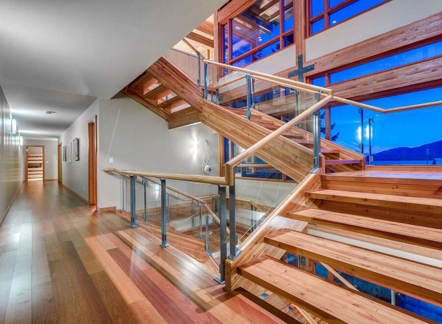 This stunning home boasts a grand wooden staircase with glass railings, offering breathtaking views through expansive windows.