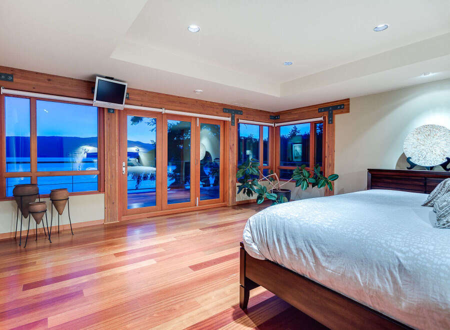 This luxurious bedroom boasts stunning lake views from its wall-to-wall windows and glass doors, creating a bright and airy atmosphere.