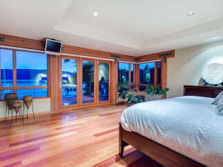 This luxurious bedroom boasts stunning lake views from its wall-to-wall windows and glass doors, creating a bright and airy atmosphere.