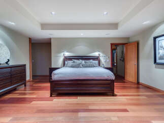 This luxurious bedroom boasts a king-size bed with plush bedding, complemented by hardwood floors and recessed lighting.