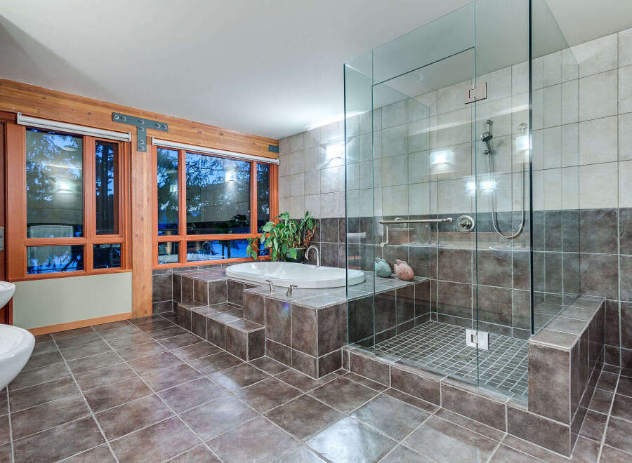 This luxurious bathroom boasts a spacious walk-in shower with glass enclosure and built-in seating, complemented by a modern freestanding bathtub set on a raised platform.