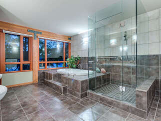 This luxurious bathroom boasts a spacious walk-in shower with glass enclosure and built-in seating, complemented by a modern freestanding bathtub set on a raised platform.
