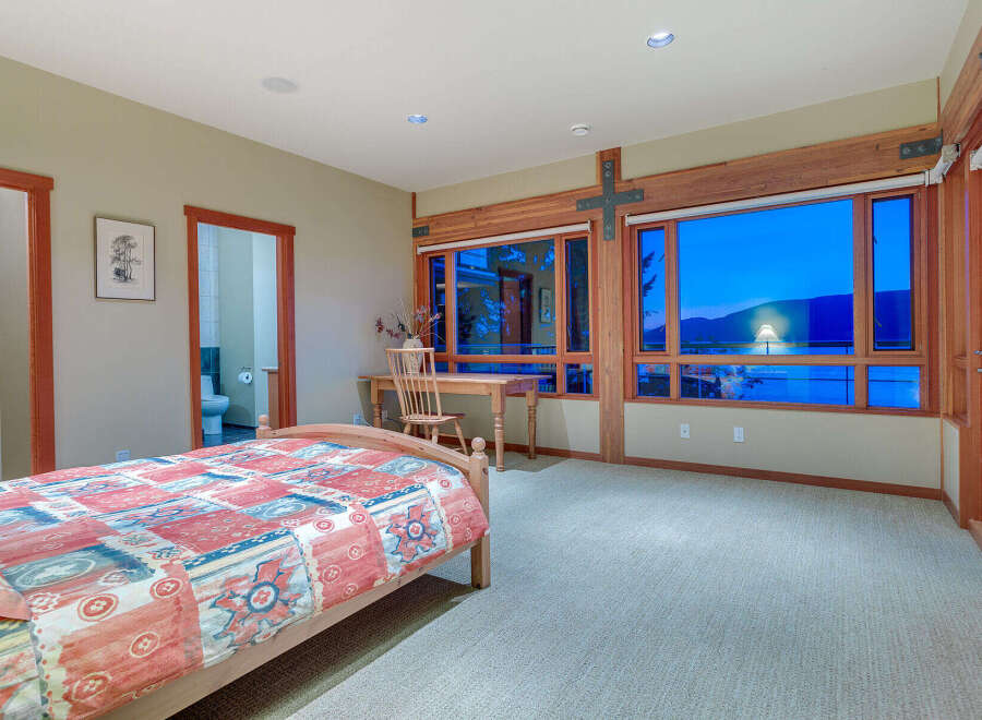 This bedroom boasts a cozy atmosphere with its hardwood floors and large windows offering stunning sunset views.