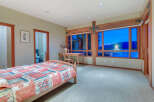 This bedroom boasts a cozy atmosphere with its hardwood floors and large windows offering stunning sunset views.