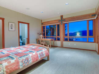 This bedroom boasts a cozy atmosphere with its hardwood floors and large windows offering stunning sunset views.