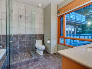 This luxurious bathroom boasts a spacious walk-in shower with glass enclosure and modern fixtures, complemented by dark brown and light beige tiles.