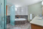 This luxurious bathroom boasts a spacious corner bathtub with glass enclosure, complemented by dark brown and light gray tile flooring.