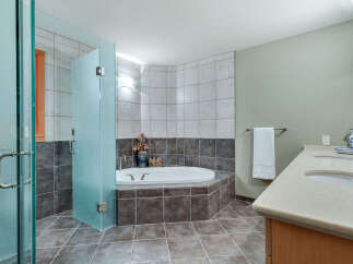 This luxurious bathroom boasts a spacious corner bathtub with glass enclosure, complemented by dark brown and light gray tile flooring.