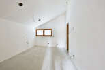This unfinished room features a sloped ceiling with recessed lighting, a large window providing ample natural light, and exposed wiring indicating ongoing renovations.