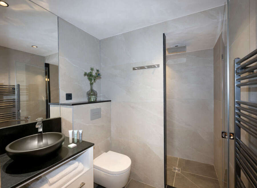 Modern bathroom with a sleek black sink, white toilet, and a walk-in shower.