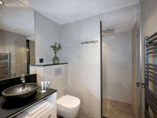 Modern bathroom with a sleek black sink, white toilet, and a walk-in shower.