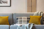 Cozy living room with a grey sofa featuring mustard yellow and grey patterned throw pillows, a light teal throw blanket, and a framed mountain landscape print on the wall.