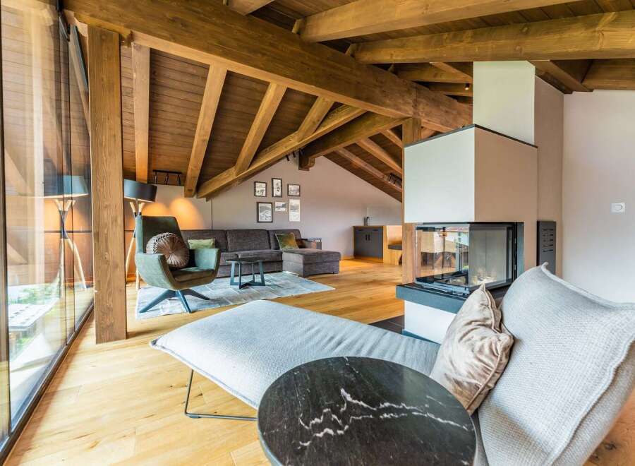 This stunning chalet boasts a spacious open-plan living area with exposed wooden beams, large windows offering breathtaking views, and a cozy fireplace as a focal point.