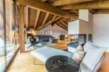 This stunning chalet boasts a spacious open-plan living area with exposed wooden beams, large windows offering breathtaking views, and a cozy fireplace as a focal point.