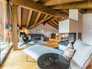 This stunning chalet boasts a spacious open-plan living area with exposed wooden beams, large windows offering breathtaking views, and a cozy fireplace as a focal point.