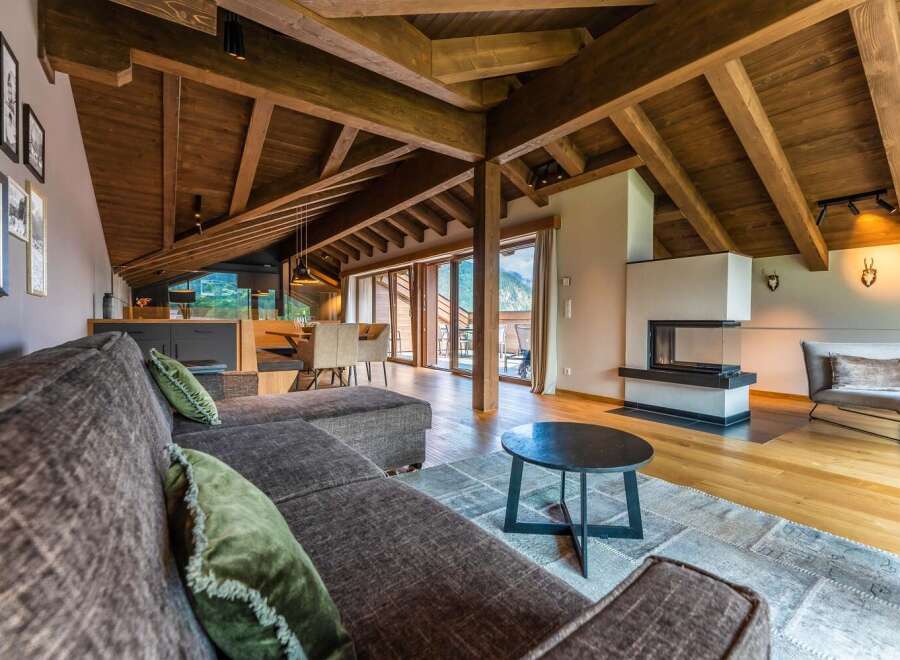This stunning chalet boasts a spacious open-plan living area with exposed wooden beams, a cozy fireplace, and large windows offering breathtaking mountain views.