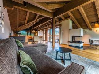 This stunning chalet boasts a spacious open-plan living area with exposed wooden beams, a cozy fireplace, and large windows offering breathtaking mountain views.