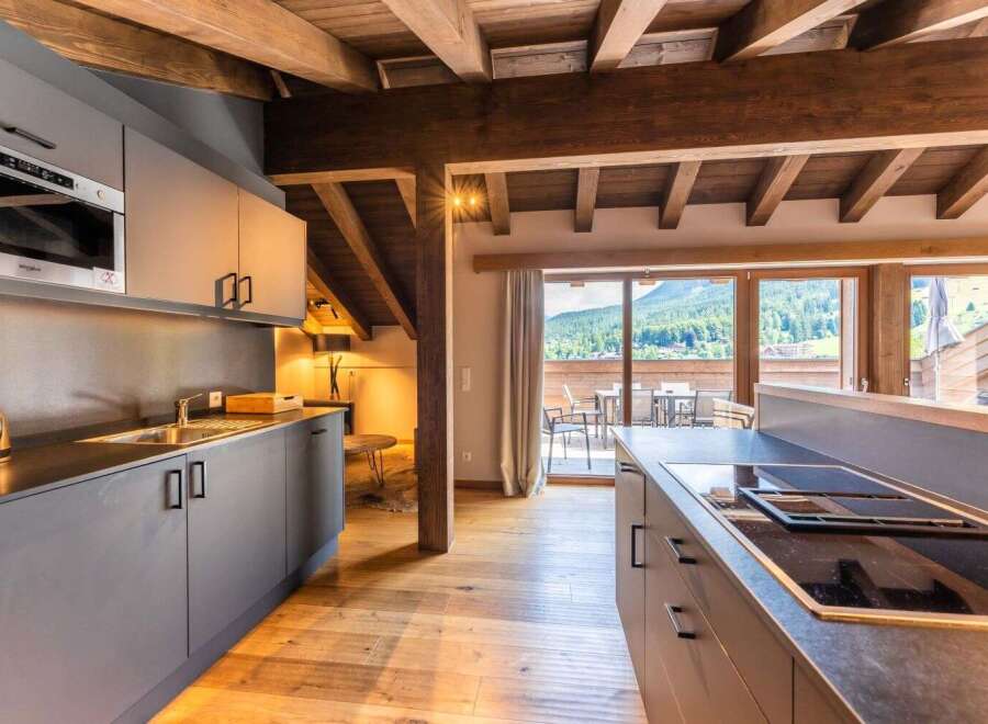 This stunning apartment boasts a modern kitchen with sleek gray cabinetry, integrated appliances, and a breakfast bar, perfect for enjoying meals while taking in the breathtaking mountain views.