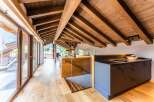 This stunning penthouse boasts a spacious open-plan living area with exposed wooden beams, large windows offering breathtaking mountain views, and a modern kitchen with sleek dark cabinetry.