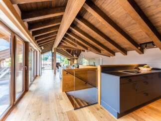This stunning penthouse boasts a spacious open-plan living area with exposed wooden beams, large windows offering breathtaking mountain views, and a modern kitchen with sleek dark cabinetry.