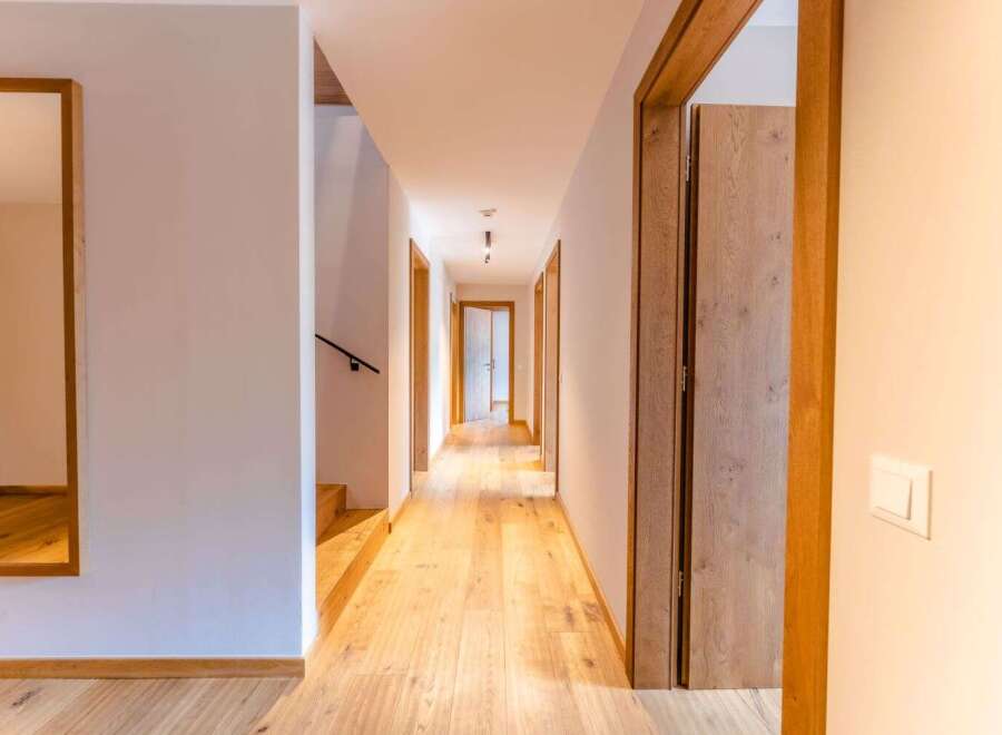 This stunning hallway boasts light oak hardwood flooring, complemented by sleek, modern wooden doors and light walls.