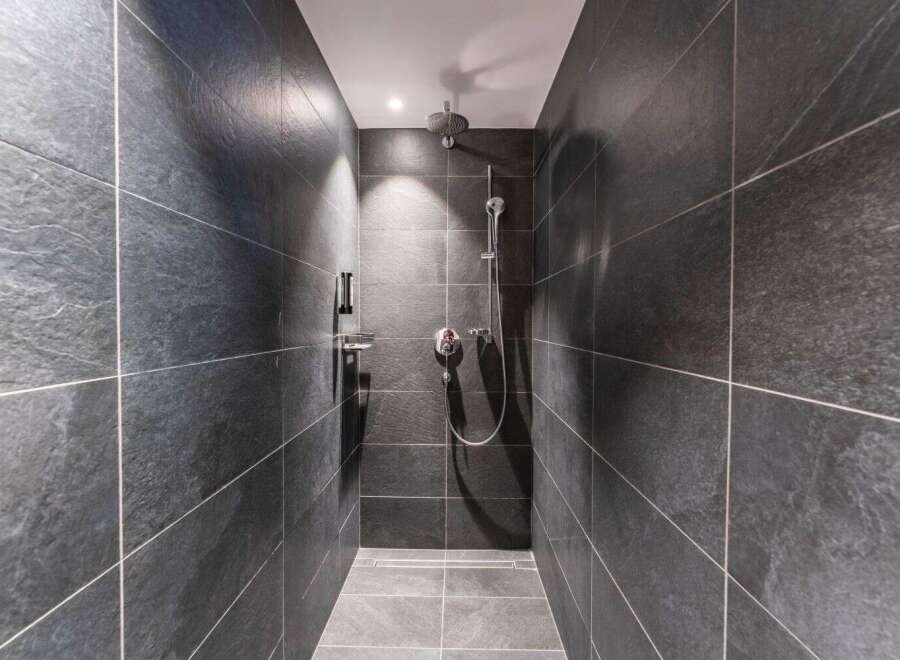 This modern shower features sleek, dark gray slate tiles creating a sophisticated and minimalist aesthetic.
