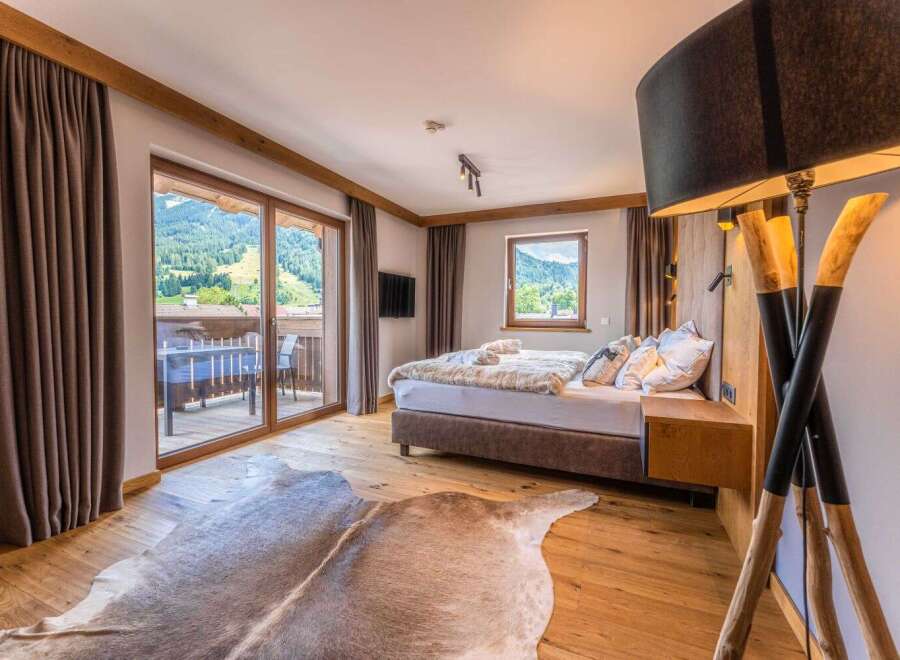 This luxurious bedroom boasts stunning mountain views from its private balcony, accessible through large sliding glass doors.