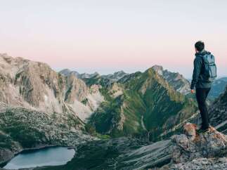 A hiker stands on a rocky outcrop, gazing out at a breathtaking vista of rolling green and grey mountains.