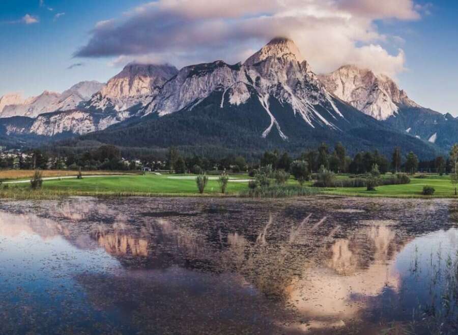Picturesque landscape featuring a serene lake reflecting majestic mountains under a vibrant sunset sky.